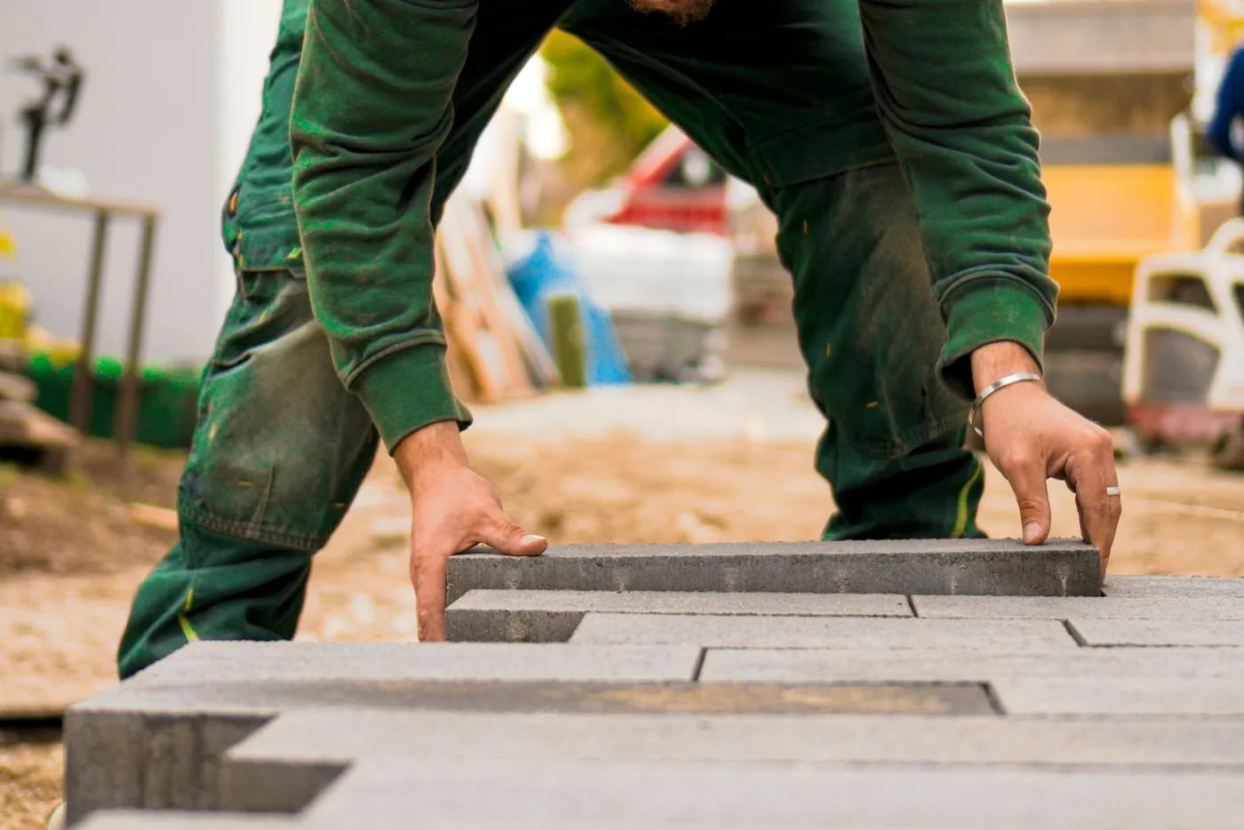 Gloved hands setting grey concrete pavers in place on a prepared base