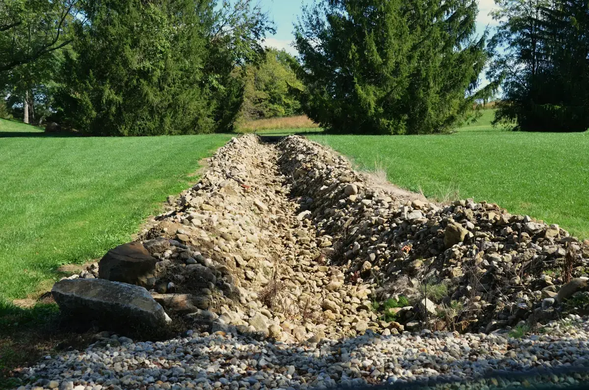 A drainage trench lined with gravel, dug across a lawn to carry water away