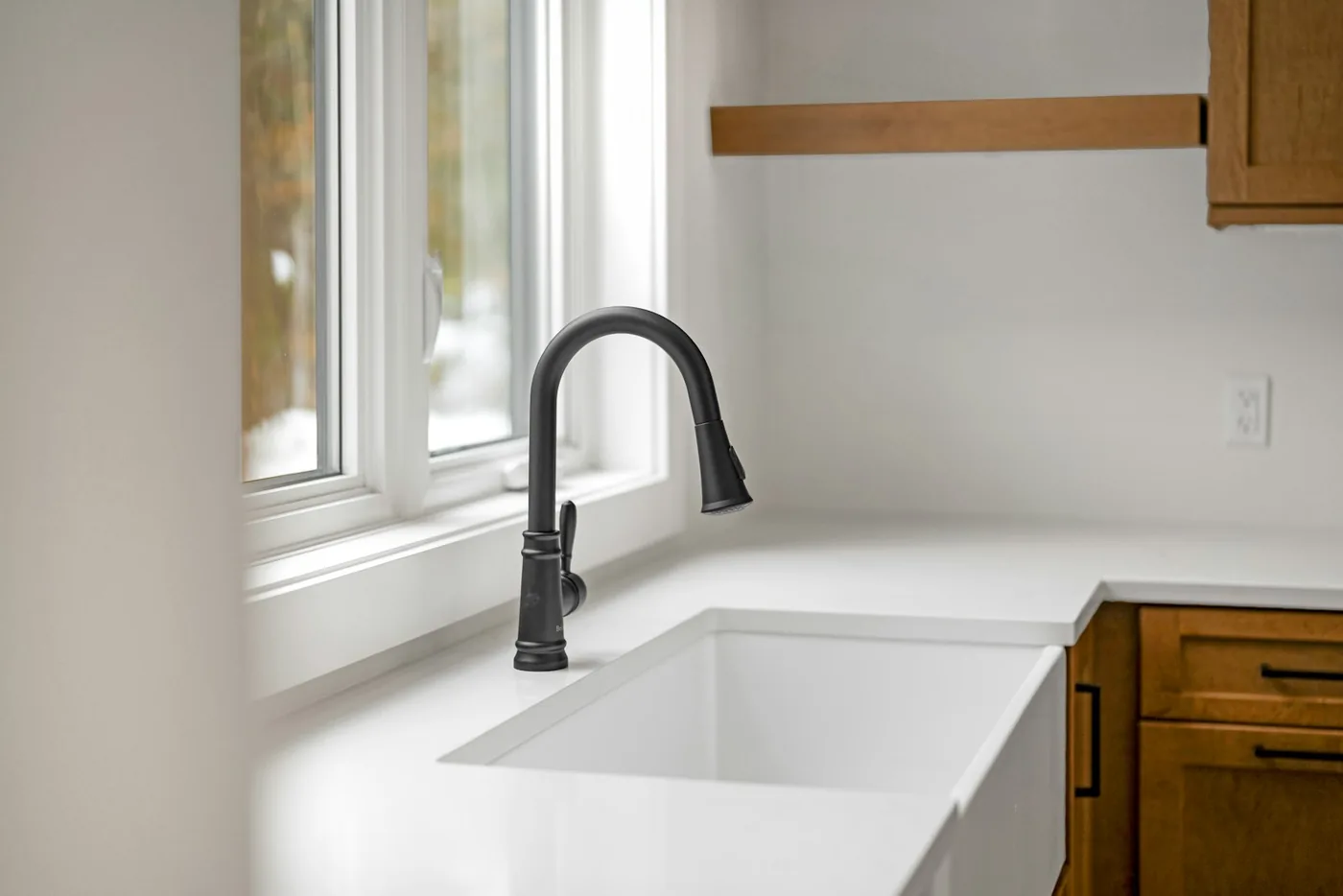 A newly installed black pull-down faucet over a white farmhouse kitchen sink